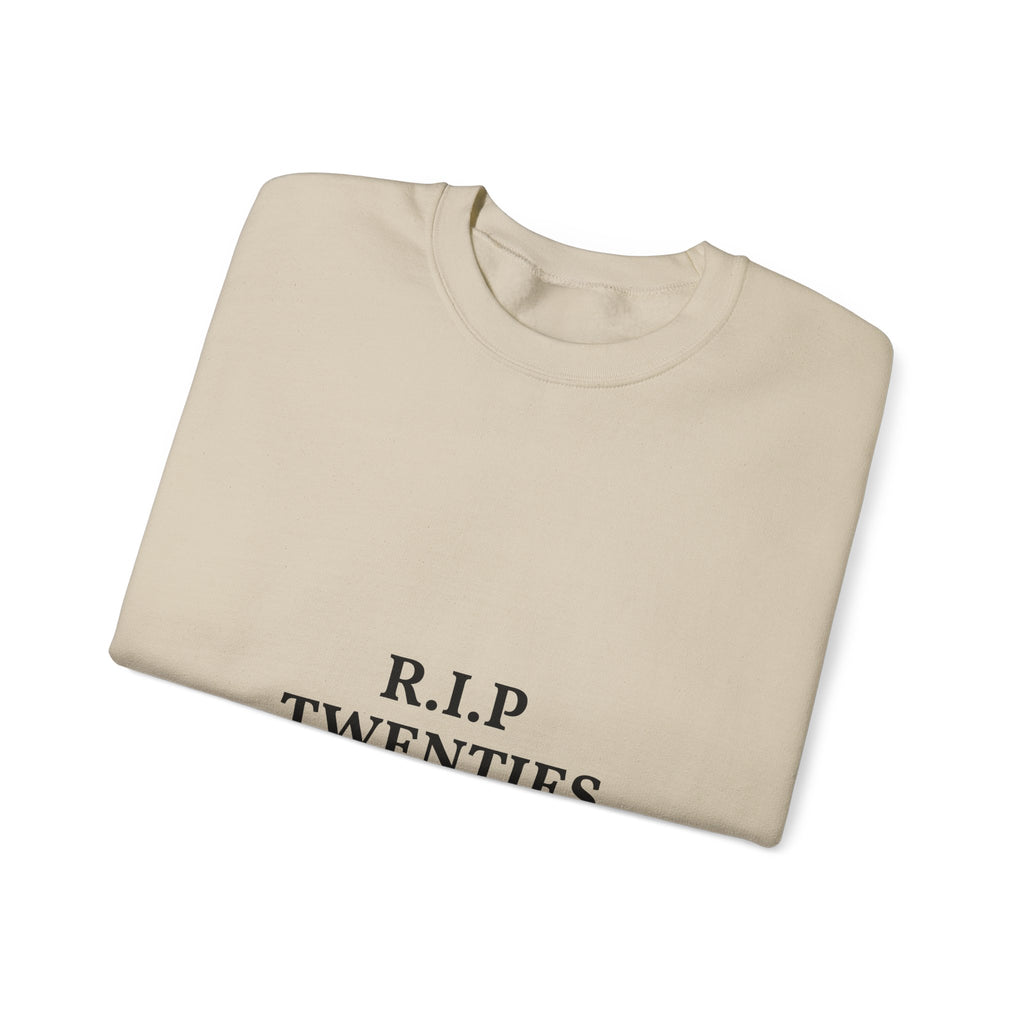 Folded beige sweatshirt with 'R.I.P. TWENTIES' text on a white background